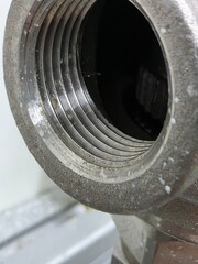 Close-up view of a metallic pipe fitting showcasing intricate threading and surface texture, highlighting industrial design and engineering craftsmanship in a workshop environment