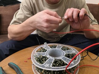 Male technician repairing New Year's garland with intricate wiring, surrounded by tools and festive decorations, showcasing the holiday spirit and craftsmanship