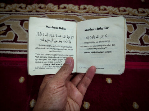 a hand holding a pocket book containing prayers and dhikr
