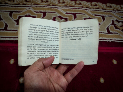 a hand holding a pocket book containing prayers and dhikr