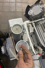 Air compressor maintenance technician hand holding nut during repair of industrial machinery. Close-up of desiccant air dryer filter and motor cooling fins in a professional workshop environment.