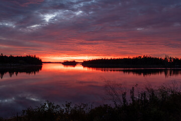 Mystical autumn sunrise on Nova Scotia’s Atlantic coast near Halifax, where soft morning red glows through clouds above calm water, creating a serene coastal mood.