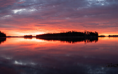 Obraz premium Mystical autumn sunrise on Nova Scotia’s Atlantic coast near Halifax, where soft morning red glows through clouds above calm water, creating a serene coastal mood.