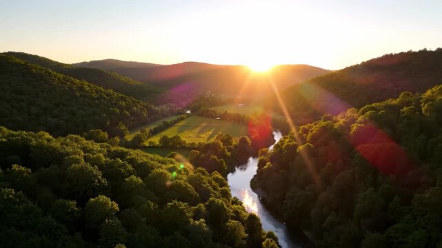 The sun rises majestically over the lush green hills, casting golden light across the serene river. This tranquil landscape showcases vibrant trees and open fields beneath a clear sky.