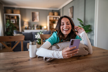 Woman laughing while communicating on smartphone at home