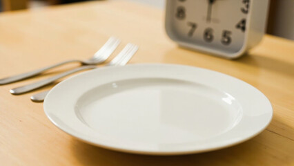 Empty plate and forks on wooden table with clock in background, mealtime concept