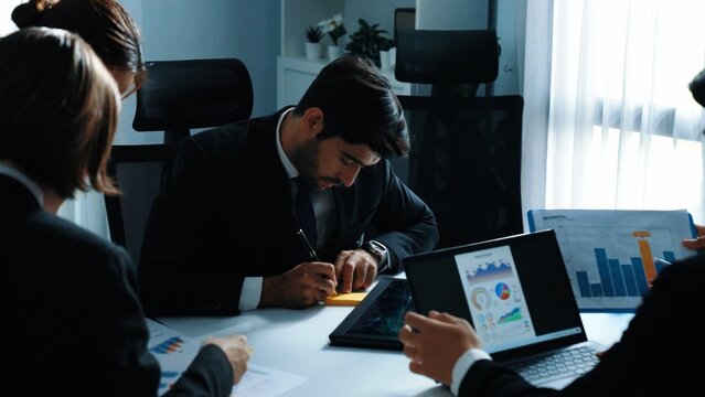 Back view of businessman working on laptop while team analysis data. Skilled marketing team writing marketing idea at meeting room. Group of diverse people brainstorm financial idea. Directorate. - Powered by Adobe
