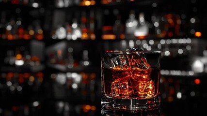 A glass of whiskey on ice with garnish, set against an indoor bar background.