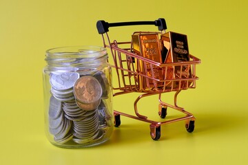 trolley containing gold bars and coins in a jar with a yellow background