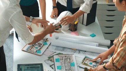 Smart architect or civil engineer writing building structure idea on note and stick on blueprint. Aerial view of manager working together with diverse colleague and show house plan. Alimentation.