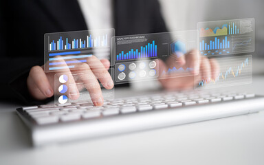 A business professional engages with digital data displays while typing on a computer keyboard,...