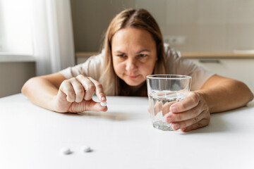 Woman focusing on white pill while holding a glass of water, preparing to take medication for headache, depression, or daily treatment