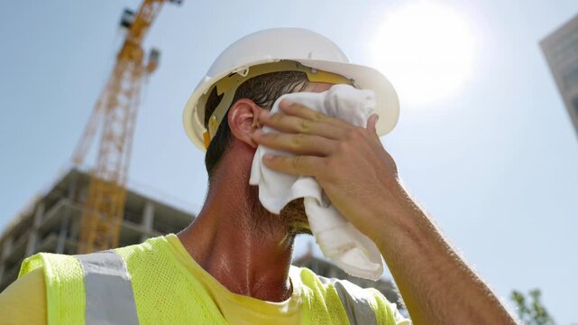 A construction worker wipes sweat from his brow on a hot day at a construction site.