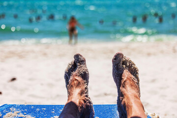 Close up view of sandy male feet resting on beach lounger with blurred in turquoise Atlantic sea. Miami Beach. USA.