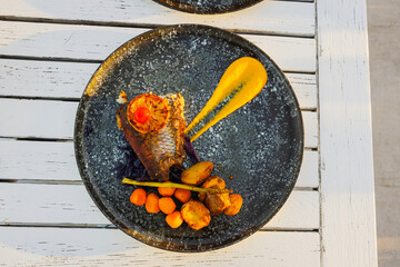 Close-up view of gourmet fried fish fillet with vegetables and sauce served in restaurant on black plate. Curacao.