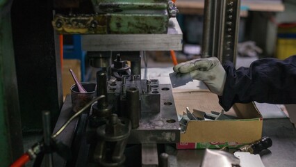 Industrial worker preparing metal parts at press machine in small manufacturing factory
