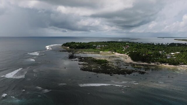 Dark cloudy sky over surf reef break with surfers paddling in shallow coastal water. Cloud 9 Surfing Area. Siargao, Philippines.