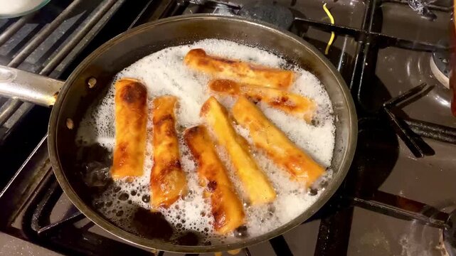 Spring rolls deep frying in a pan of hot oil