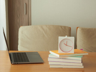 家のリビングの机の上にあるノートパソコンと本と時計の様子