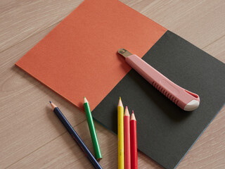 色画用紙の上にあるたくさんのカラフルな色鉛筆とカッターナイフの様子