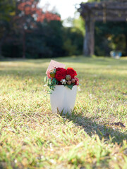 秋の昼の公園の芝生にある白い花瓶と鮮やかな造花の様子