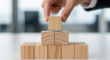 Wooden cubes representing leadership structure being positioned manually with fine shallow focus and softly diffused background