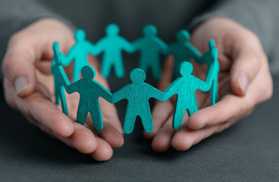 Hands holding teal wooden cutout figures representing unity and teamwork, emphasizing cooperation and community support