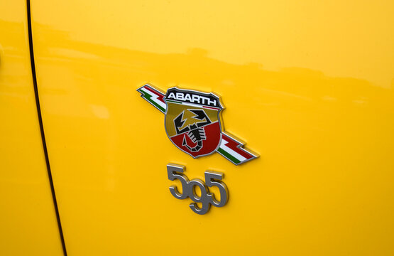 Close up of the Abarth shield logo and 595 model designation badge on the bright, glossy yellow body panel of a car, showing the vibrant Italian racing colors
