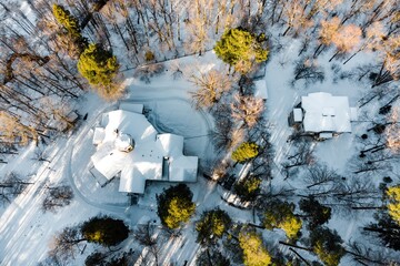 Aerial drone view captures snow-covered roofs of suburban homes nestled within a bright winter forest setting