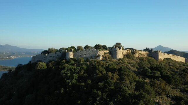 Aerial view of the historic Navarino Castle ruins surrounded by lush greenery and overlooking the sea in Greece. Scenic Mediterranean landscape with mountains and coastline in the background.