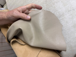 A person holds a piece of beige leather in a crafting workshop while working on a project