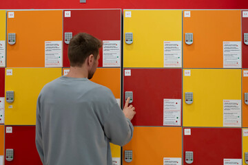 A man stands in front of lockers, pressing buttons on a keypad to open a locker