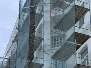 Workers repair a building's outer walls with scaffolding and nets on a cloudy day