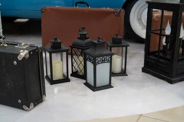 Lanterns and old suitcases are placed on the floor near a classic car in an indoor space