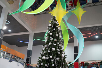 A large Christmas tree is decorated with ornaments in a shopping center with colorful decor
