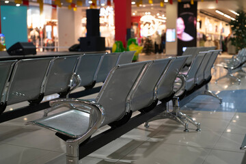 People walk by as metal chairs sit empty in a shopping mall waiting area