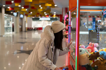Girl focuses on a claw machine filled with colorful stuffed animals in a mall