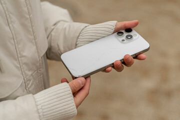A person stands outside holding a smartphone that has a cracked screen in their hand