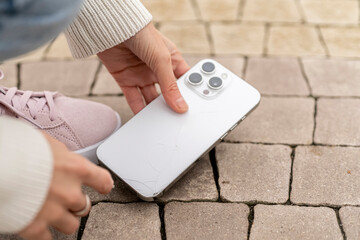 A person reaches down to grab a smartphone that fell on the ground in daylight