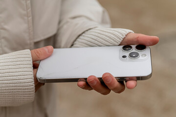 A person is holding a smartphone in their hand while standing in a neutral outdoor area