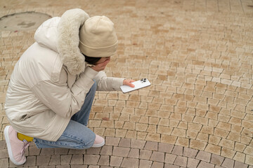 A person is crouching on a stone path while checking their smartphone in a public space