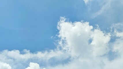Naklejka premium A beautiful summer day features fluffy white cumulus clouds drifting across a clear blue sky, creating a bright and natural cloudscape within the sunny atmosphere.