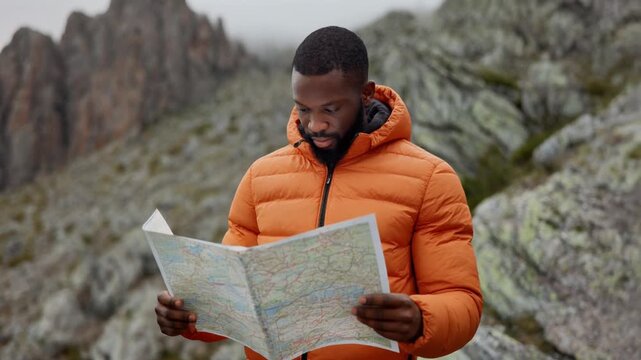 Person in bright orange puffy jacket holds detailed map for new adventure. Hiker plans mount.