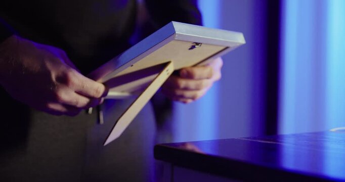 Moody close-up of hands holding a picture frame under blue lighting&mdash;concept for sadness, grief, loss, memories, and emotional reflection.