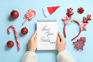 Woman with notebook for New Year Goals 2026 and Christmas decor on blue background