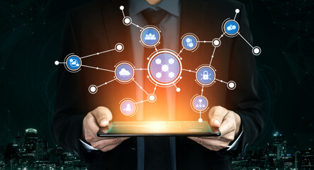 A businessman in a suit holds a tablet displaying digital icons connected through a network, symbolizing modern technology and communication in an urban landscape. Tessel