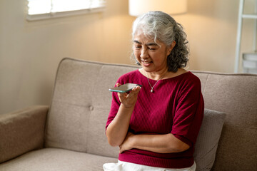 Older Asian woman use smartphone voice assistant talking home living room sofa communication technology mobile device interaction comfort relaxed
