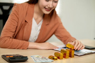 Asian adult business investor woman managing gold bar assets personal finance for wealth growth on office desk