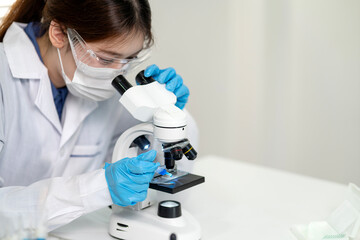Asian female scientist researcher using microscope examining biological sample conducting experiment in modern laboratory for scientific discovery healthcare innovation