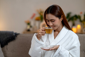 Adult Asian woman enjoying warm herbal tea in white bathrobe at home spa setting for serene self care and relaxation moment